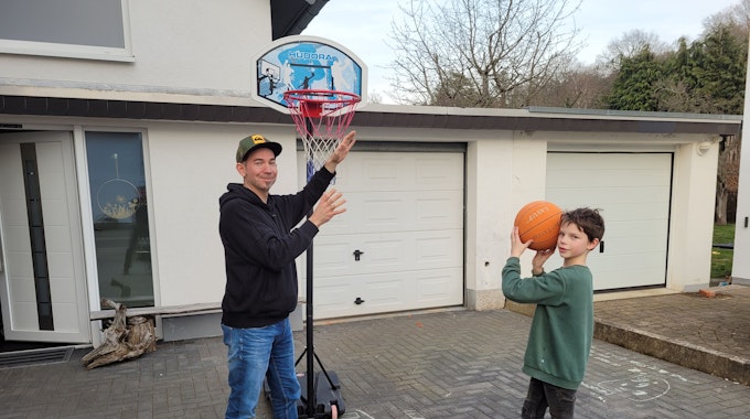 Nick Mertens steht mit seinem Vater in der Einfahrt und spielt Basketball.