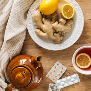Auf einem Tisch stehen eine Teekanne, eine Teetasse mit Tee, Honig und ein Teller mit Ingwer und Zitrone.