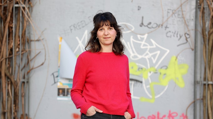 Leonie Pfennig trägt einen pinken Pullover und steht vor einer Wand mit Graffitis.&nbsp;&nbsp;
