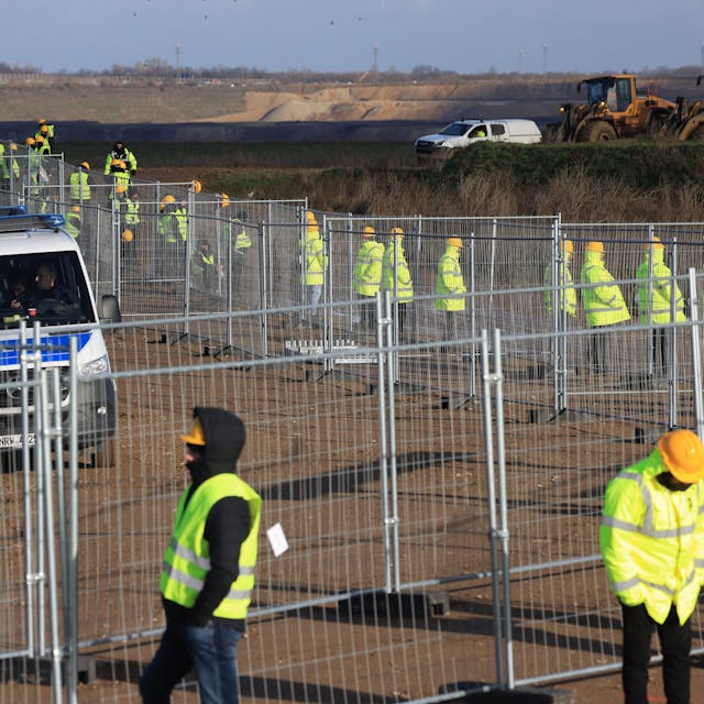 Mitarbeiter einer Werkschutzfirma stehen im Januar an einem Zaun beim von Klimaaktivisten besetzten Braunkohleort Lützerath. Sie alle tragen neongelbe Warnjacken. Hinter dem Zaun sind Vans der Polizei zu sehen.&nbsp;