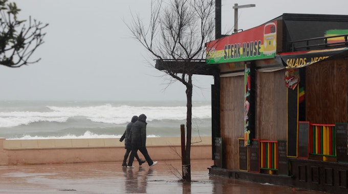Ein Paar geht bei stürmischem Wetter an der Strandpromenade von Can Picafort spazieren. Für die nächsten Tage wird Regen mit niedrigen Temperaturen erwartet.