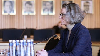 Ministerin Ina Scharrenbach (CDU) ist im Halbprofil zu sehen; sie sitzt am Mikrofon, trägt einen dunkelblauen Blazer und einen beigen Rollkragenpullover. Sie schaut ihr Gegenüber konzentriert an.