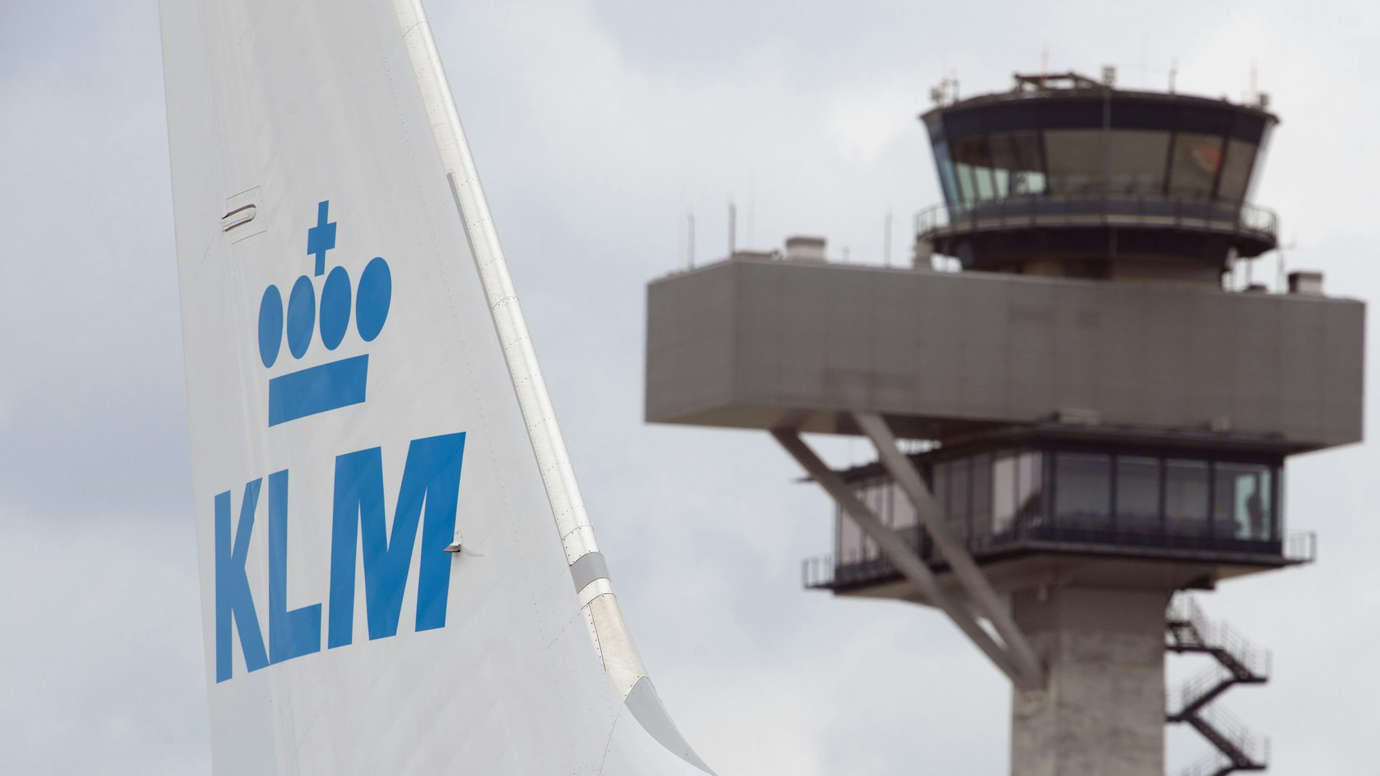 Eine Boeing 737 der niederländischen Fluggesellschaft KLM steht auf einem Rollfeld. Im Hintergrund ist ein Flughafen-Tower zu sehen.