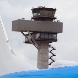 Eine Boeing 737 der niederländischen Fluggesellschaft KLM steht auf einem Rollfeld. Im Hintergrund ist ein Flughafen-Tower zu sehen.