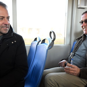 Fußball-Bundestrainer Hansi Flick (l.) und Handball-Bundestrainer Alfred Gislason sitzen zusammen in einer Straßenbahn.