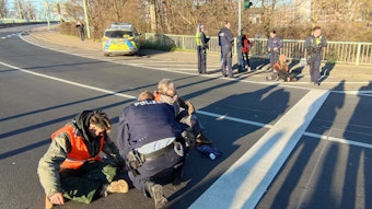 Zwei Aktivisten sitzen auf der Fahrbahn, ein Polizist kniet vor ihnen.
