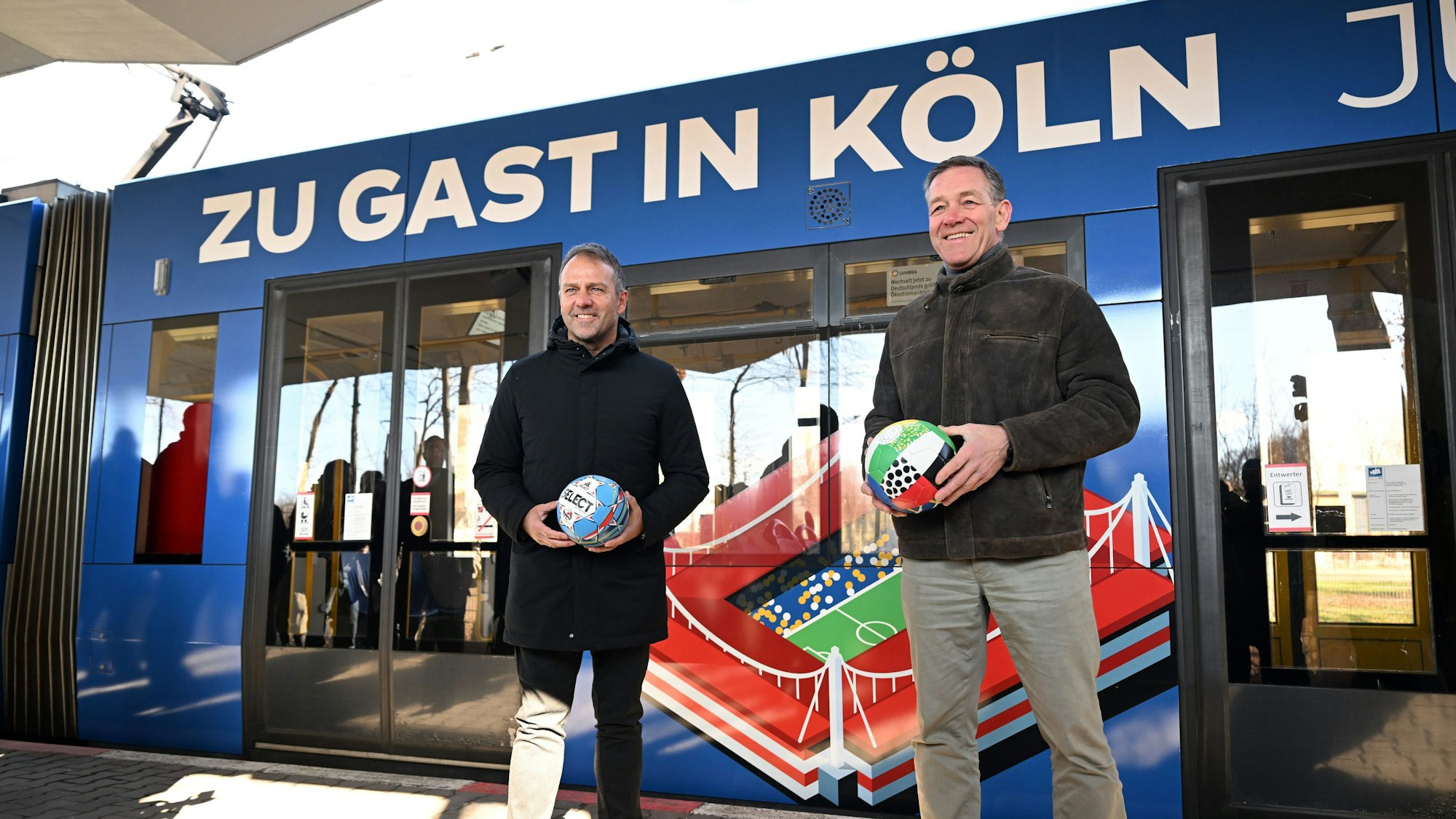 Fußball-Bundestrainer Hansi Flick (l) und Handball-Bundestrainer Alfred Gislason stehen vor einer Straßenbahn mit dem Design der Fußball-EM 2024 und der Handball-EM 2024.