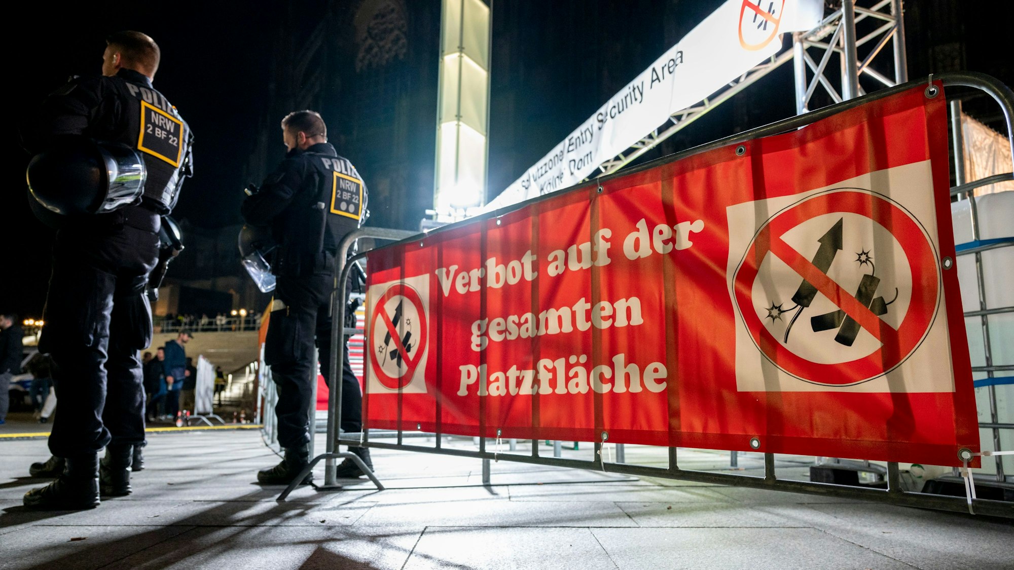 Zwei Polizisten vor einem Schild mit der Aufschrift „Verbot auf der gesamten Platzfläche“ und Böllersymbolen