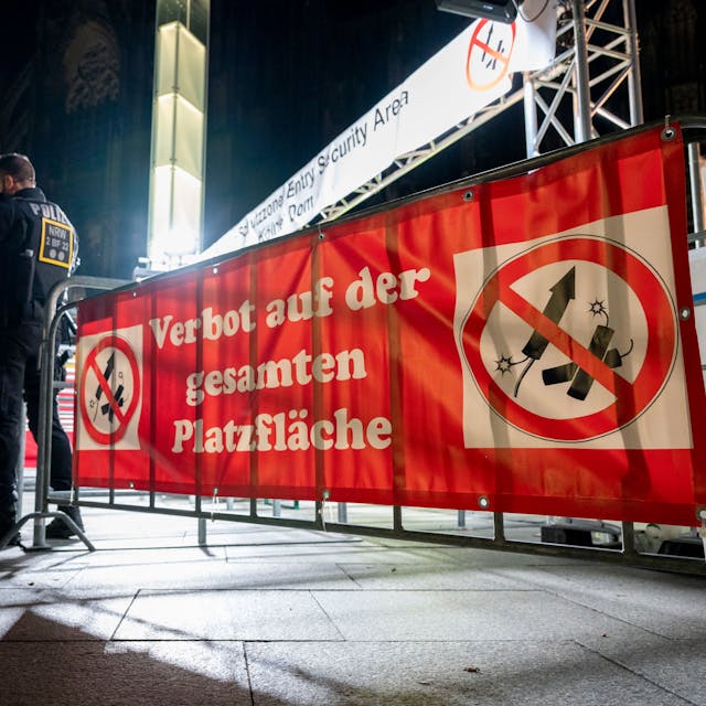 Zwei Polizisten vor einem Schild mit der Aufschrift „Verbot auf der gesamten Platzfläche“ und Böllersymbolen