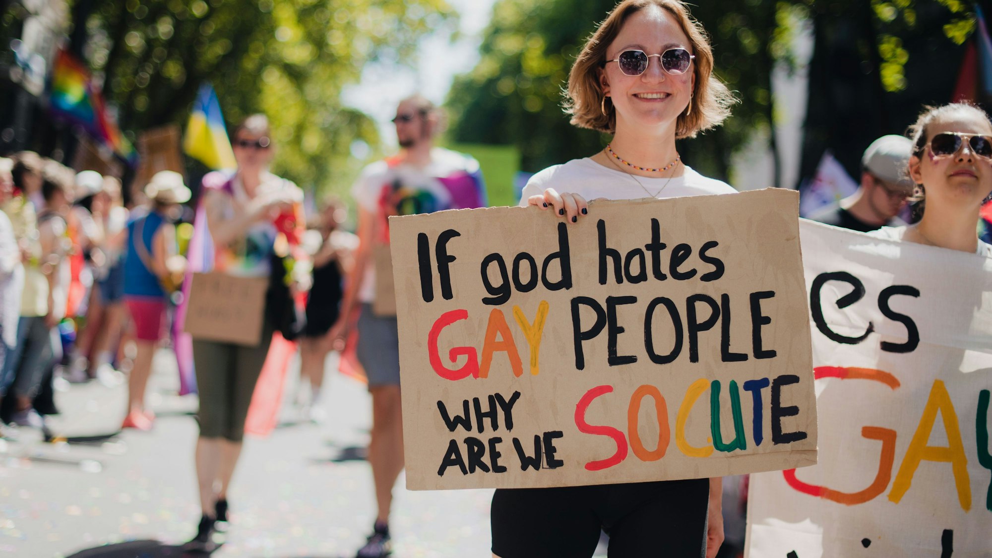 Frau mit Schildmit der Aufschrift „If god hates gay people, why are we so cute“.