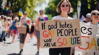 Frau mit Schildmit der Aufschrift „If god hates gay people, why are we so cute“.