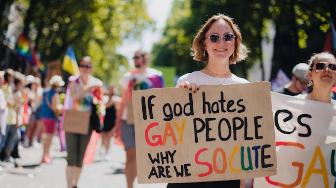 Frau mit Schild&nbsp;mit der Aufschrift „If god hates gay people, why are we so cute“.