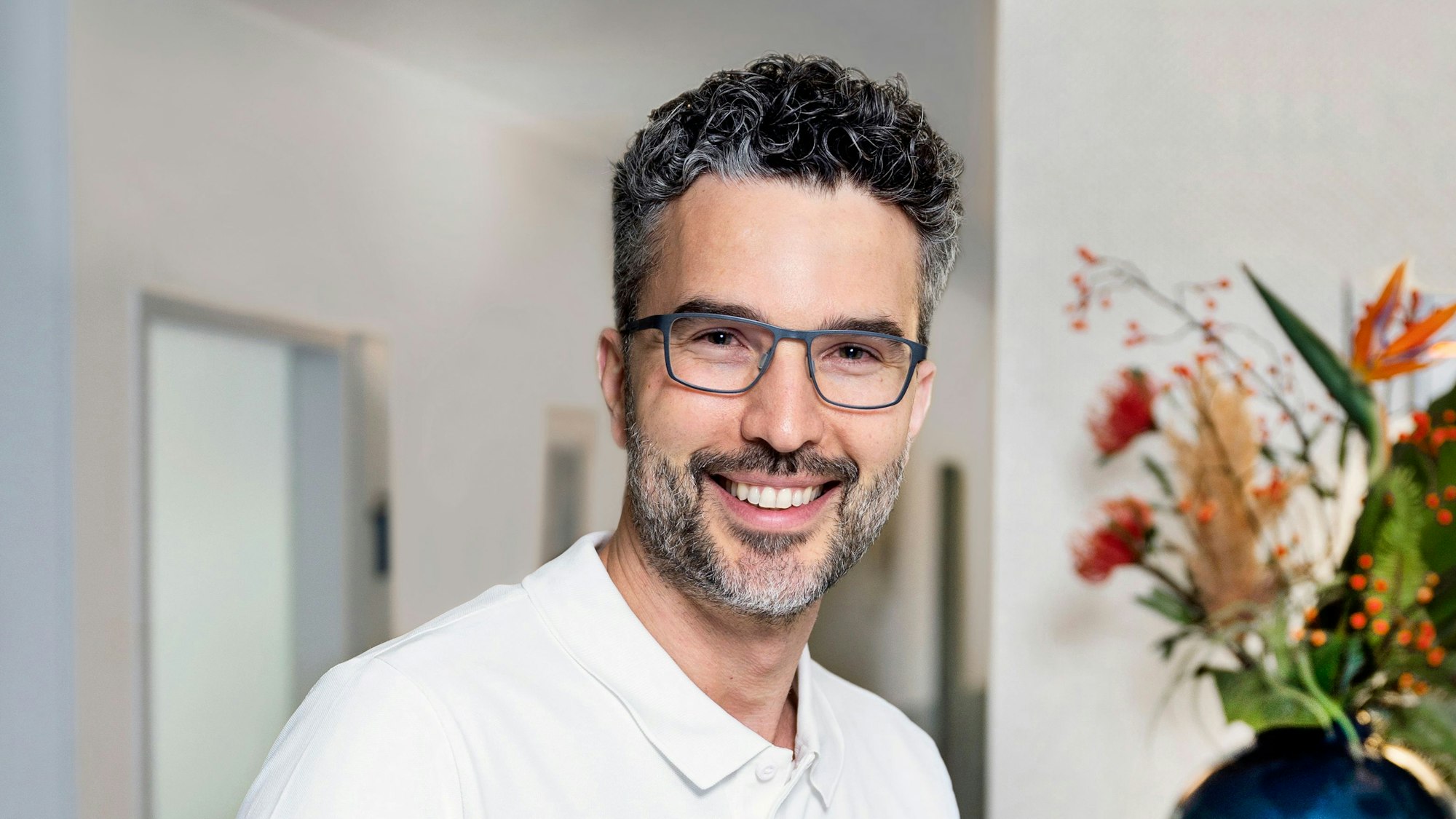Christian Levejohann ist Zahnarzt in Köln und „wir helfen“-Unterstützer, er hat graumelierte Locken einen graumelierten Bart und trägt eine schwarze Brille.