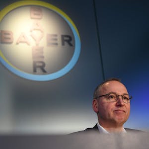 Werner Baumann sitzt in Leverkusen vor dem Bayer-Logo.