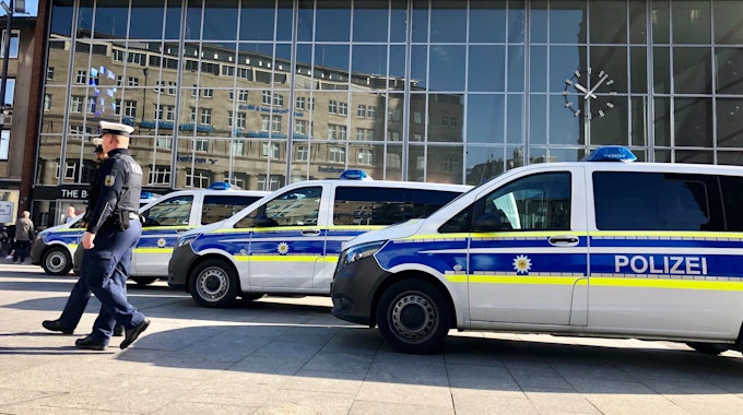 Drei Polizeiwagen stehen vor dem Kölner Hauptbahnhof. Zwei Polizisten stehen daneben.&nbsp;