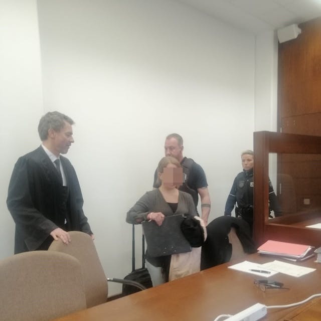Das Foto zeigt die Angeklagte im Gerichtssaal. Zu sehen sind zudem ihr Verteidiger und zwei Justizvollzugsbeamte.