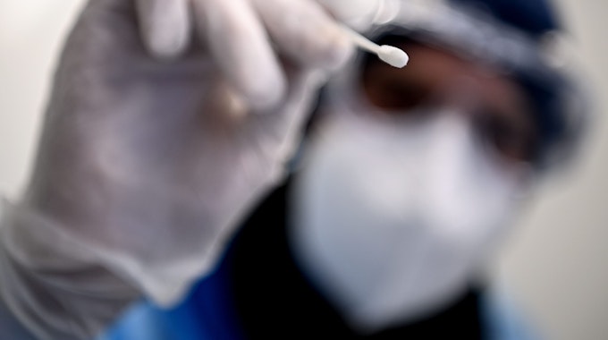 Ein Arzt hält ein Teststäbchen für die Entnahme einer Probe für einen PCR-Test in der Hand.