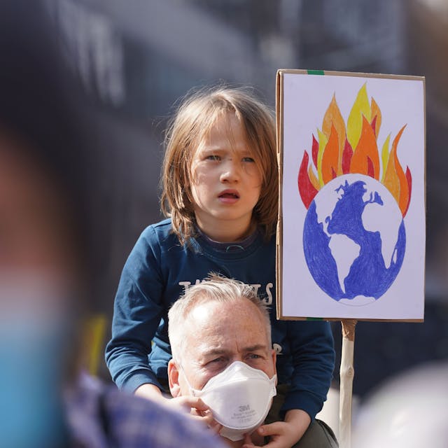 Emil sitzt auf den Schultern vom Vater Oli zwischen den Teilnehmern des Klimastreiks Fridays for Future. Der Vater hält ein Plakat mit einer brennenden Erde hoch.&nbsp;