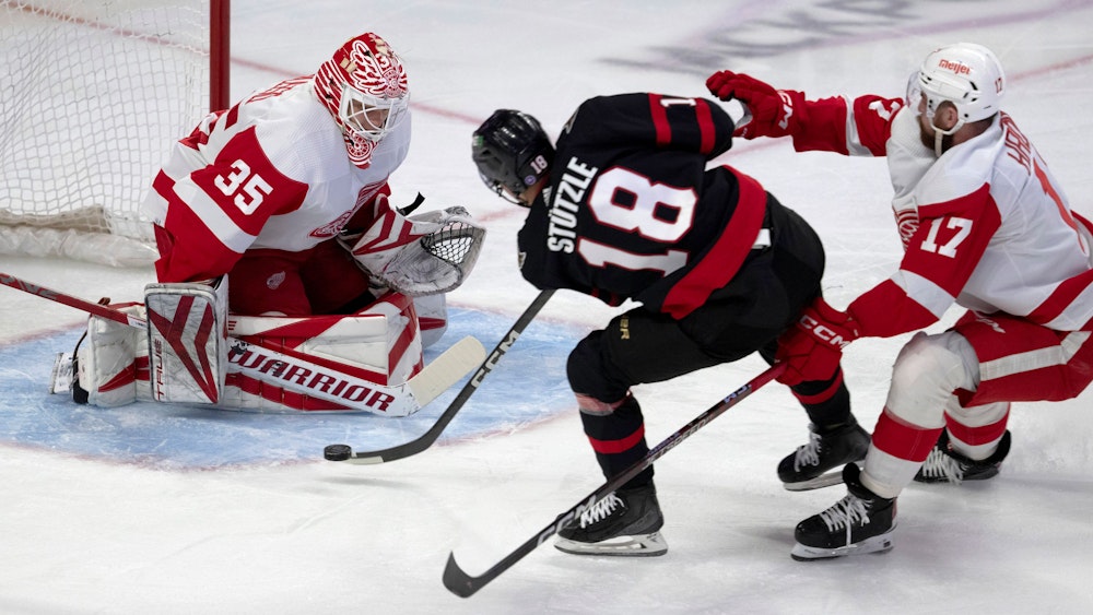 Detroit Red Wings-Verteidiger Filip Hronek (r.) verfolgt Ottawa Senators-Linksaußen Tim Stützle (M.), der den Puck auf Red Wings-Torwart Ville Husso schießt