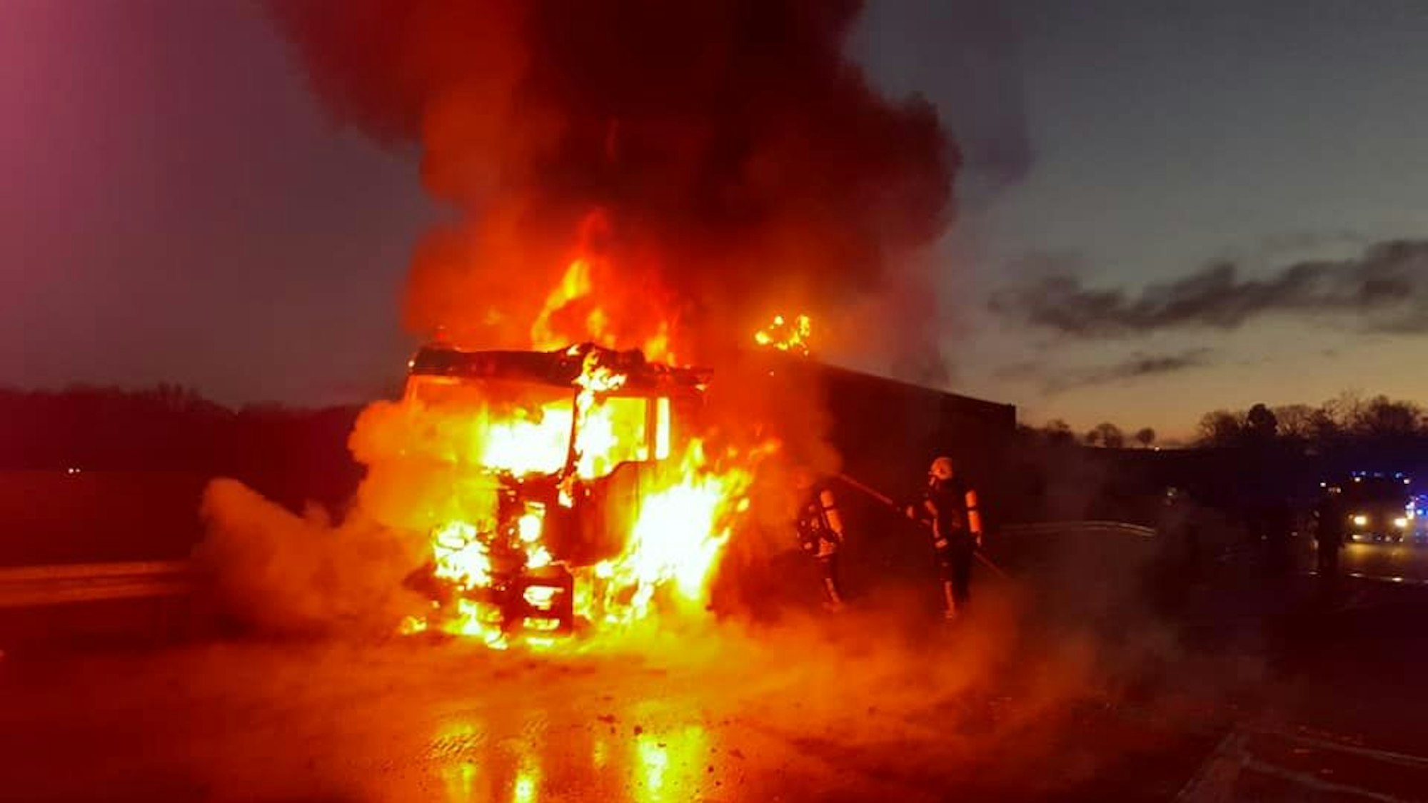 Feuerwehrleute löschen einen lichterloh brennenden Lastwagen auf der Autobahn.