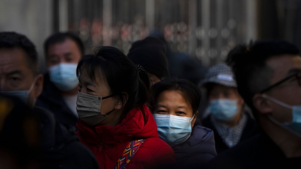Menschen tragen in einer Fußgängerzone in Peking einen Mund- und Nasenschutz.