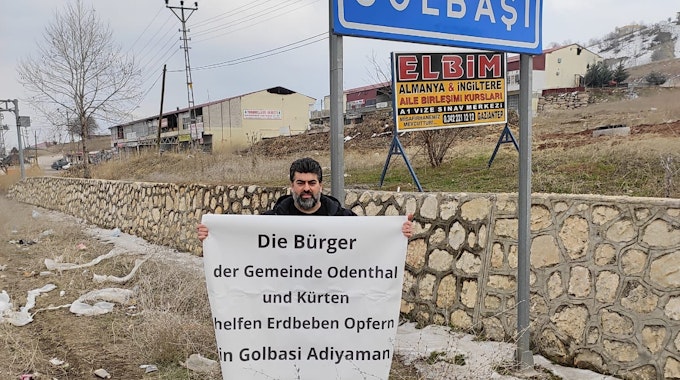 Erkan Karahan steht mit einem Banner unter dem Ortsschild von Golbasi.