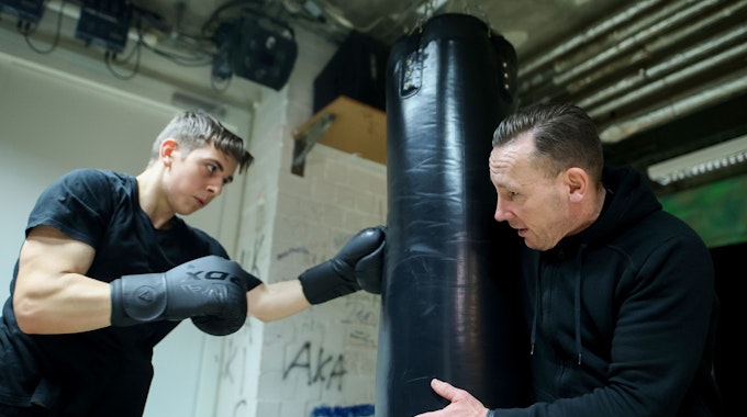 Der ehemalige Boxer René Hehne trainiert mit einem Jugendlichen an einem Sandsack.