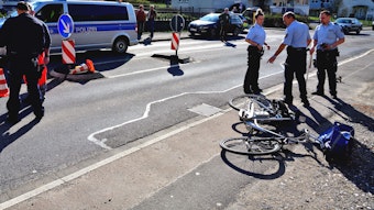 Polizisten stehen auf einer Straße, ein Rad liegt auf dem Boden.