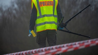 Ein Polizist untersucht einen Tatort. Er trägt eine gelbe Polizei-Weste. (Symbolbild)