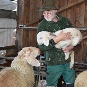 Bauer Peter Schmidt hält ein Lamm in den Armen.