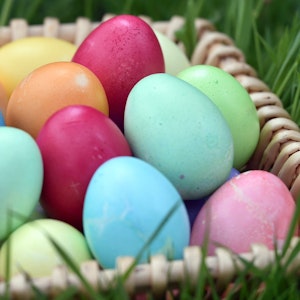Gefärbte Eier liegen in einem Körbchen auf einer Wiese.