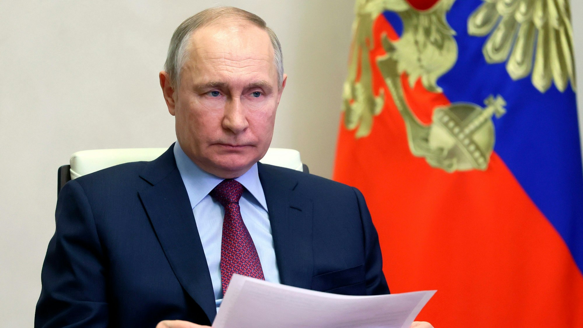 Wladimir Putin, Präsident von Russland, sitzt bei der Teilnahme an einer Videokonferenz in der Nowo-Ogarjowo-Residenz neben einer Russland-Flagge.