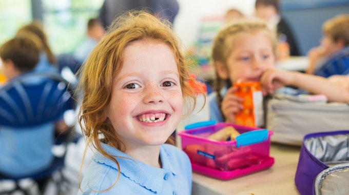 Smiling school students in uniform missing a tooth with a healthy sandwich for lunch, Foto: Getty Images/davidf