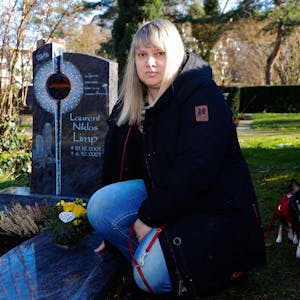 Laurents Mutter mit Hund Emmy am Grab ihres Sohnes Laurent auf dem Friedhof.