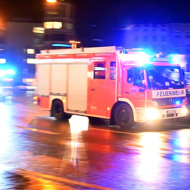 Ein Feuerwehrwagen rast im Dunkeln über eine nasse Straße.
