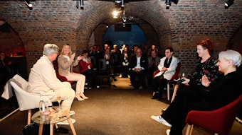 Die Teilnehmerinnen und Teilnehmer sitzen in einem gemauerten Kellergewölbe auf Sesseln.