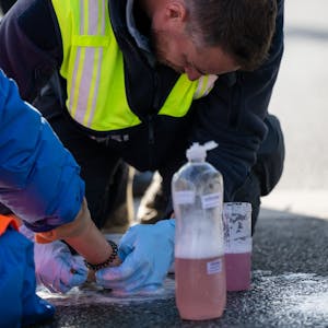 Ein Polizist löst die festgeklebte Hand eines Klimaaktivisten, der sich zuvor auf eine Straße geklebt hat.