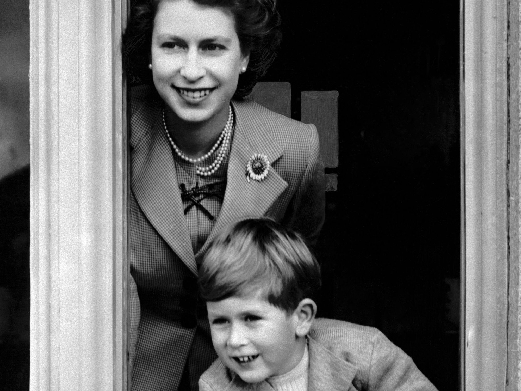 Königin Elizabeth II. und ihr Sohn, Prinz Charles, schauen aus einem Fenster.