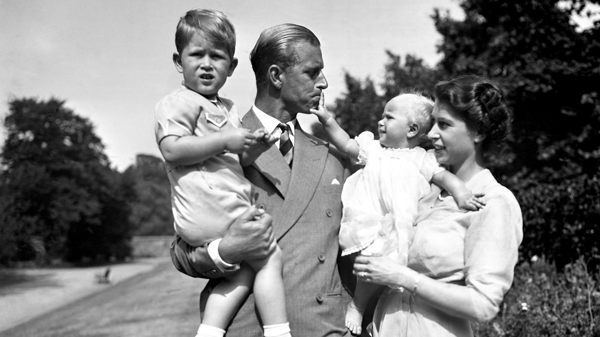 Prinzessin Elizabeth, die Prinzessin Anne in den Armen hält, und Prinz Philip, Herzog von Edinburgh, der Prinz Charles trägt, stehen auf dem Gelände von Clarence House.