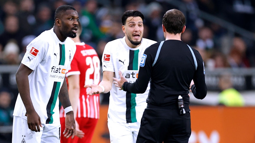 Marcus Thuram (l.) und Ramy Bensebaini (r.) diskutieren mit Schiedsrichter Benjamin Brand während der Bundesliga-Partie gegen den SC Freiburg (4. März 2023) im Borussia-Park. Beide Gladbacher sind mit einer Entscheidung nicht einverstanden.