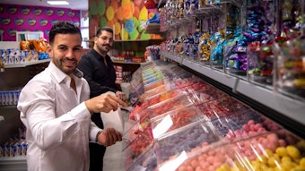 Die Betreiber des Candy Shop in Euskirchen stehen vor der Süßigkeitenwand.