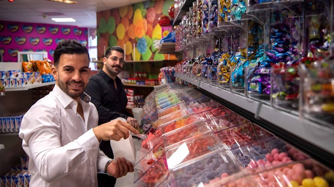 Die Betreiber des Candy Shop in Euskirchen stehen vor der Süßigkeitenwand.