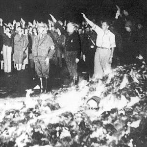 Das Archivbild zeigt eine Bücherverbrennung in Deutschland. Hinter einem brennenden Berg mit Büchern sind Menschen zu sehen, die den Hitlergruß zeigen.