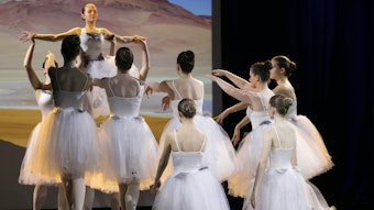 Mehrere Balletttänzerinnen tanzen auf der Bühne. Sie heben eine Tänzerin in ihrer Mitte hoch.