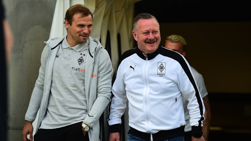 Tony Jantschke (l.) und Roland Virkus von Borussia Mönchengladbach betreten am 1. Juli 2022 den Innenraum im Stadion an der Hafenstraße vor dem Testspiel bei Rot-Weiss Essen. Beide sprechen miteinander und grinsen.