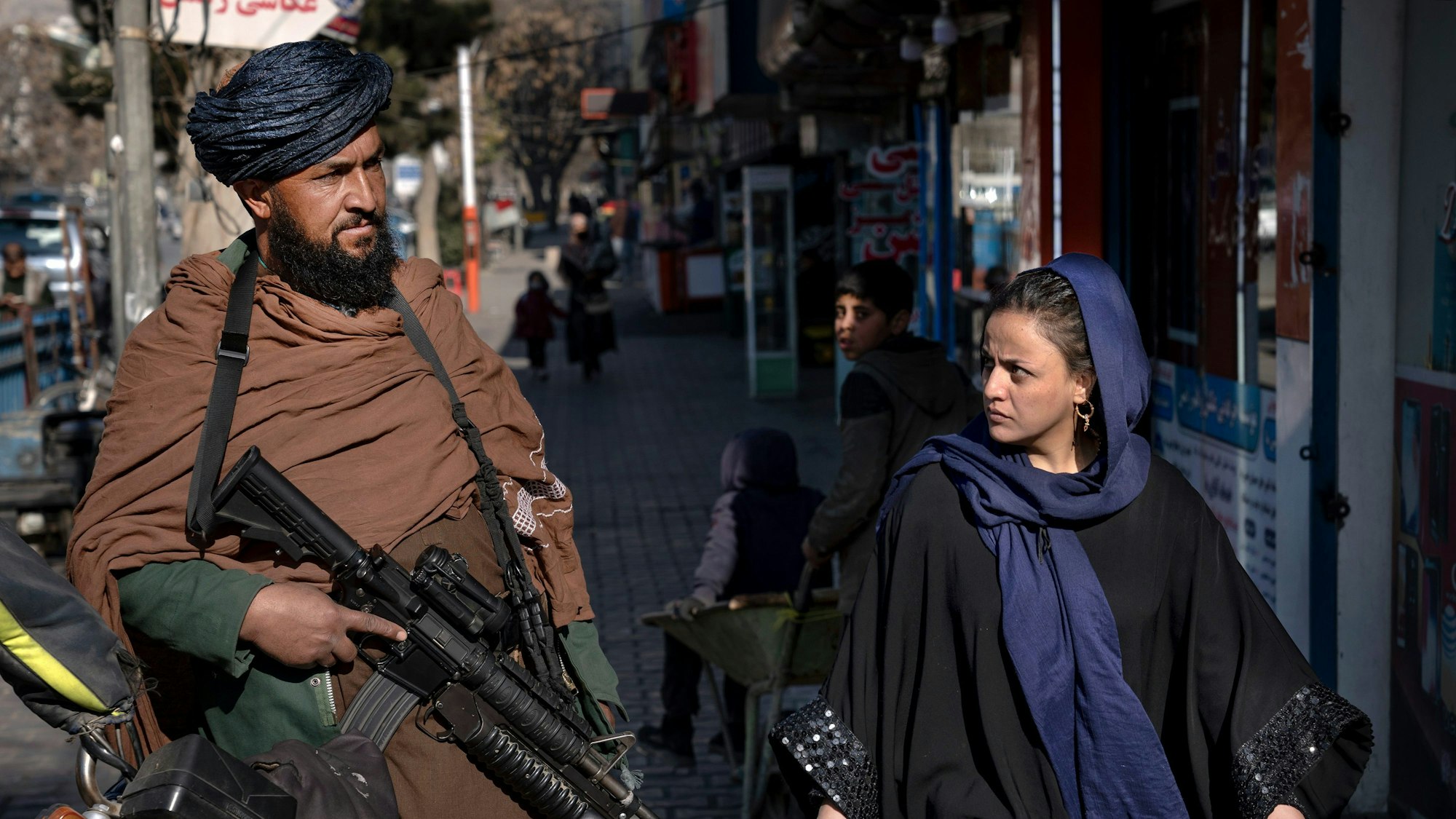 Ein Taliban-Kämpfer steht Wache, während eine Frau vorbeiläuft.