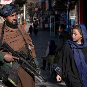 Ein Taliban-Kämpfer steht Wache, während eine Frau vorbeiläuft.
