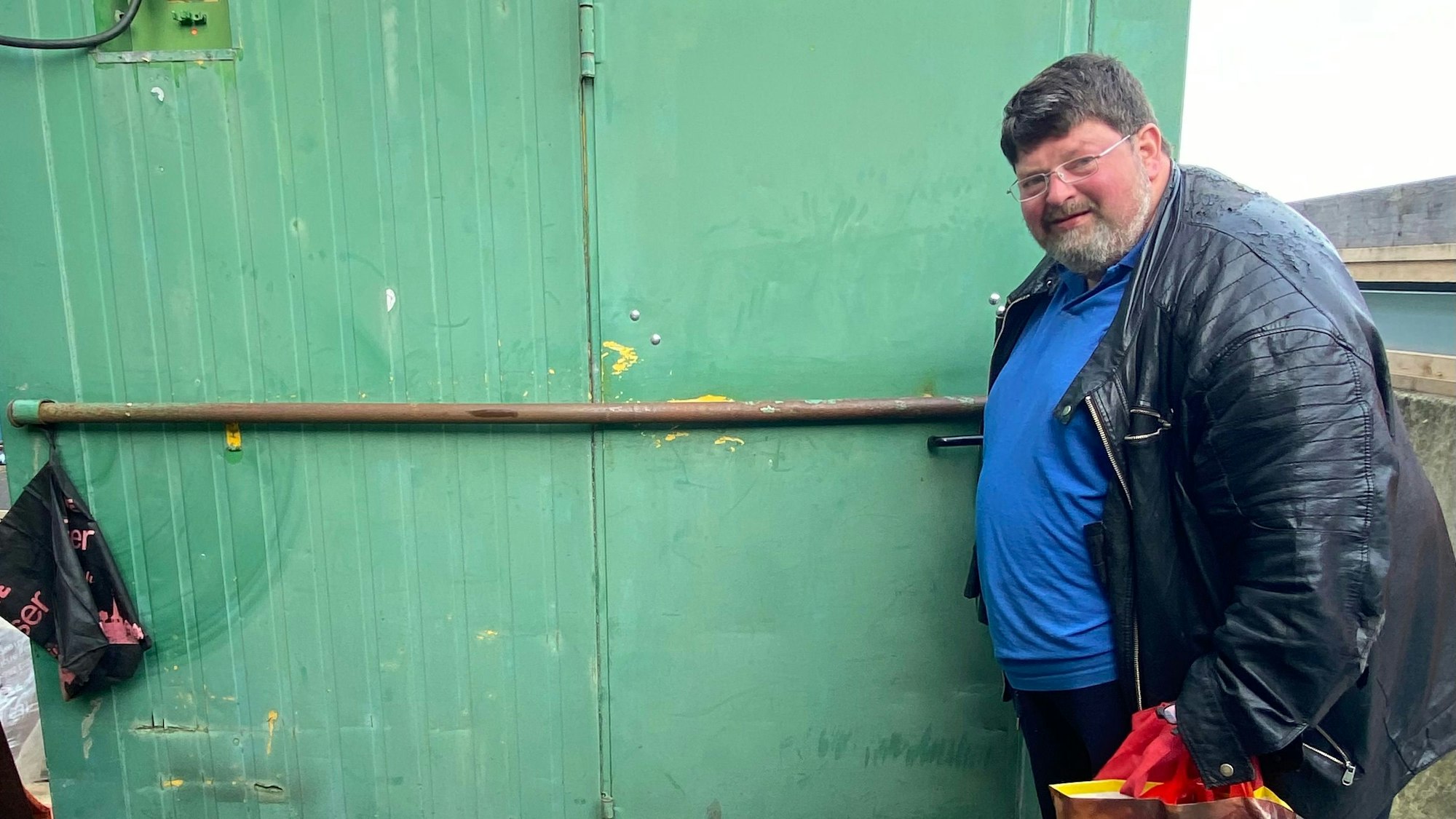 Klaus Berg an der Tür zu seinem Zuhause, er schaut in die Kamera, hinter sich eine grüne Containerwand.