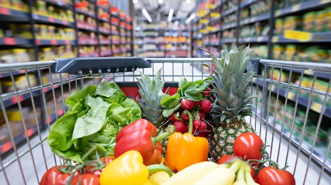 Ein Einkaufswagen mit Obst und Gemüse steht in einem Supermarkt.