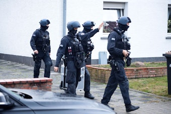 Maskierte Polizeikräfte gehen bei einer Razzia in Köln aus einem Haus heraus.